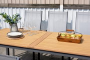 Gartentisch aus Holz mit dekorativen Elementen wie einem Krug mit Blumen, Weingläsern und einem Obstkorb, aus der Perspektive von oben betrachtet.