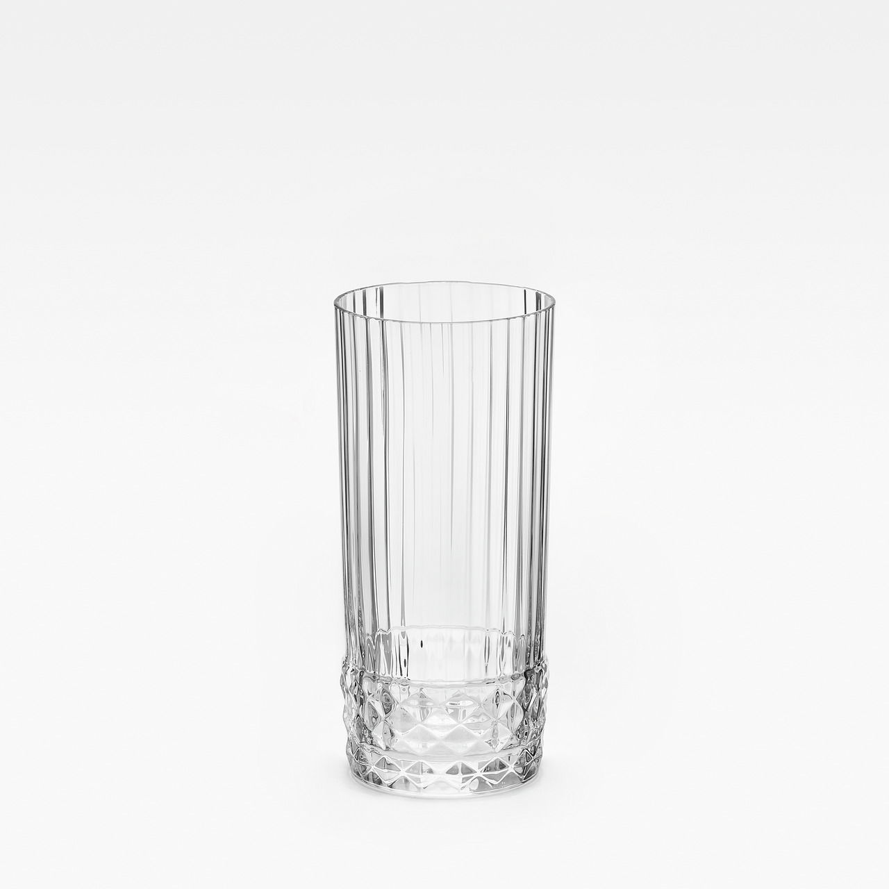 Klares Longdrinkglas mit vertikalen Rillen und facettiertem Boden, frontal fotografiert.