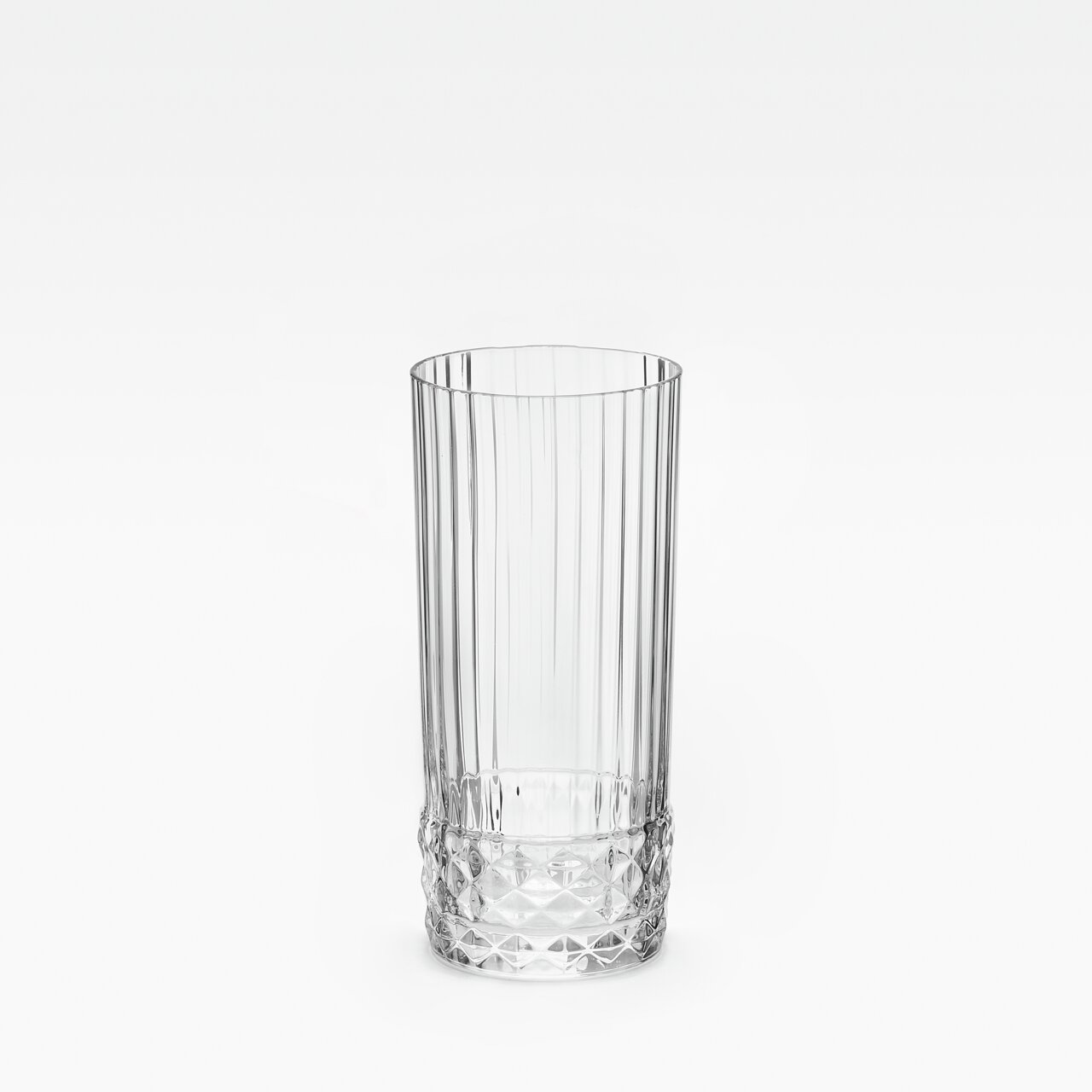 Klares Longdrinkglas mit vertikalen Rillen und facettiertem Boden, frontal fotografiert.
