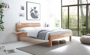Modernes Bettgestell Primeto 25 aus Holz in einem hellen, minimalistischen Schlafzimmer mit großen Fenstern und natürlichem Licht, seitliche Perspektive.