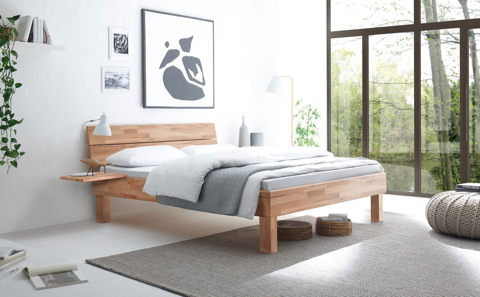 Modernes Bettgestell Primeto 25 aus Holz in einem hellen, minimalistischen Schlafzimmer mit großen Fenstern und natürlichem Licht, seitliche Perspektive.