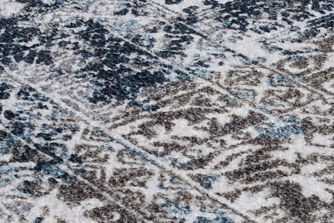 Nahaufnahme eines Teppichs mit abstraktem Muster in Blau- und Brauntönen, perspektivisch von schräg oben aufgenommen.