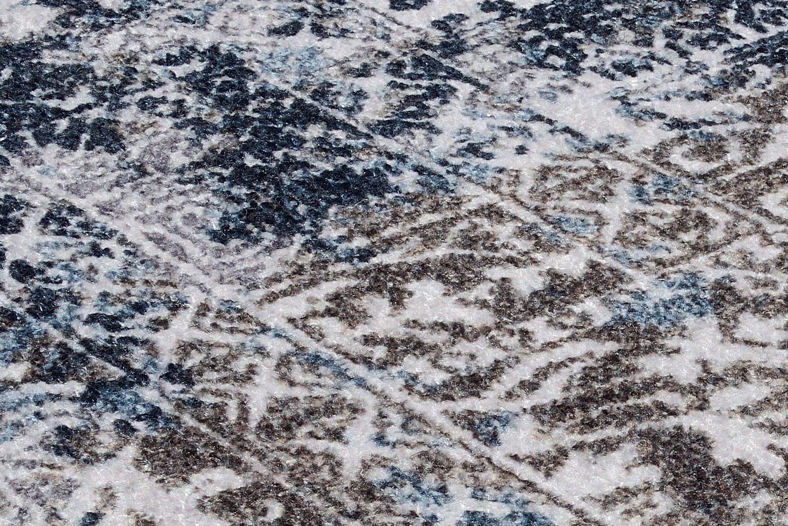 Nahaufnahme eines Teppichs mit abstraktem Muster in Blau- und Brauntönen, perspektivisch von schräg oben aufgenommen.