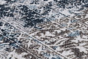 Nahaufnahme eines Teppichs mit abstraktem Muster in Blau- und Brauntönen, perspektivisch von schräg oben aufgenommen.