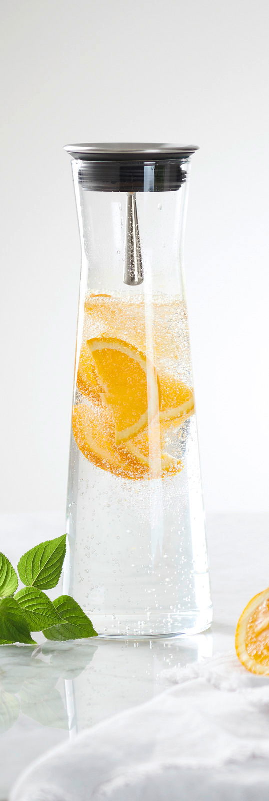 Karaffe mit 1,1 l Fassungsvermögen, gefüllt mit sprudelndem Wasser und Orangenscheiben, aus der Seitenperspektive fotografiert.