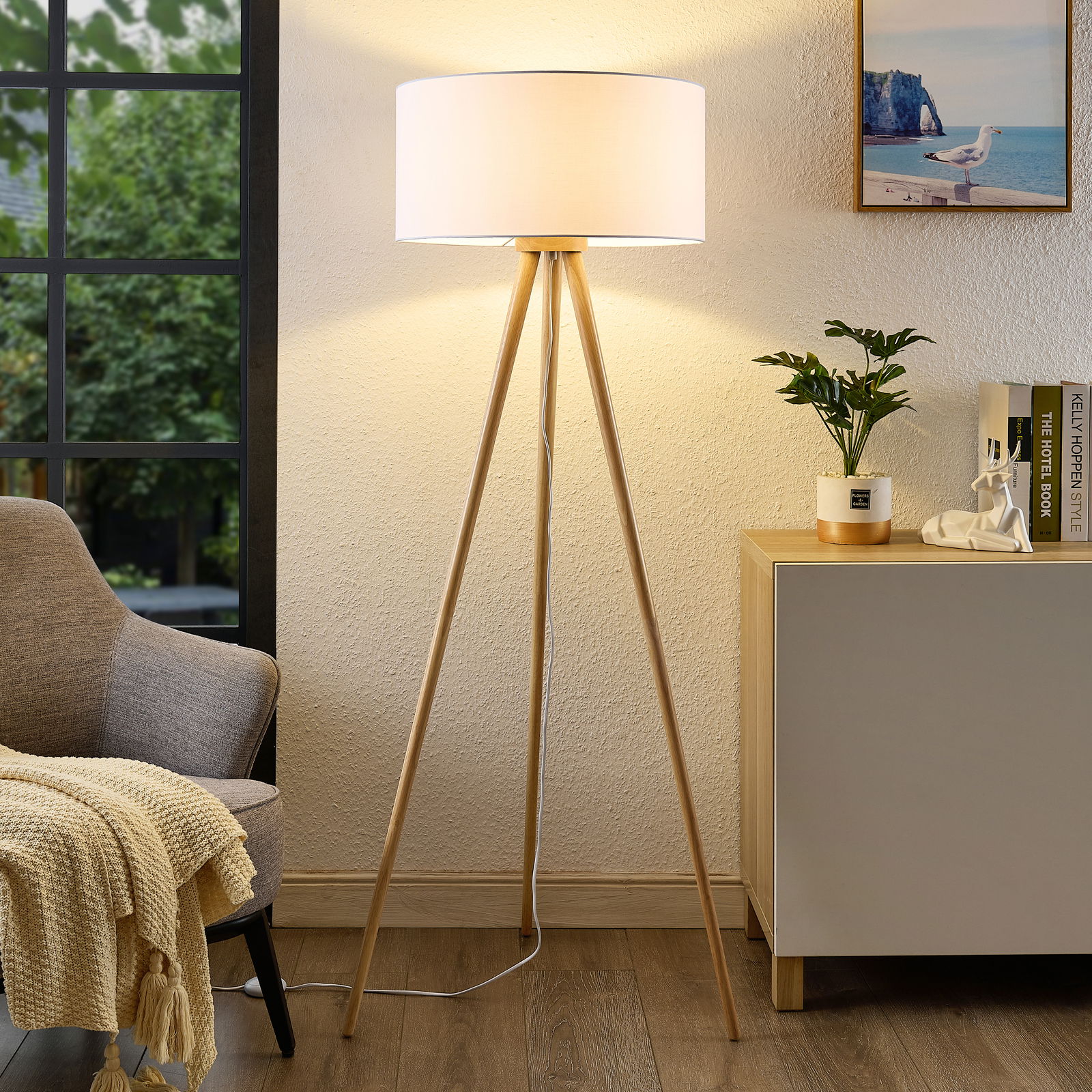 Novel Stehleuchte Moderne Stehleuchte mit dreibeinigem Holzgestell und weißem Lampenschirm, frontal im Wohnzimmer platziert.