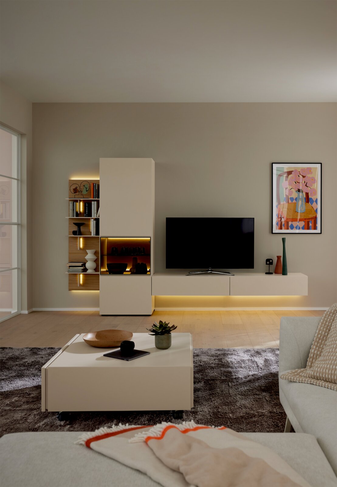 Frontansicht einer modernen, weiß-beigen Wohnwand mit TV-Lowboard, hohem Stauraumschrank, offenen Holzregalen und stimmungsvoller LED-Beleuchtung in einem stilvollen Wohnzimmer