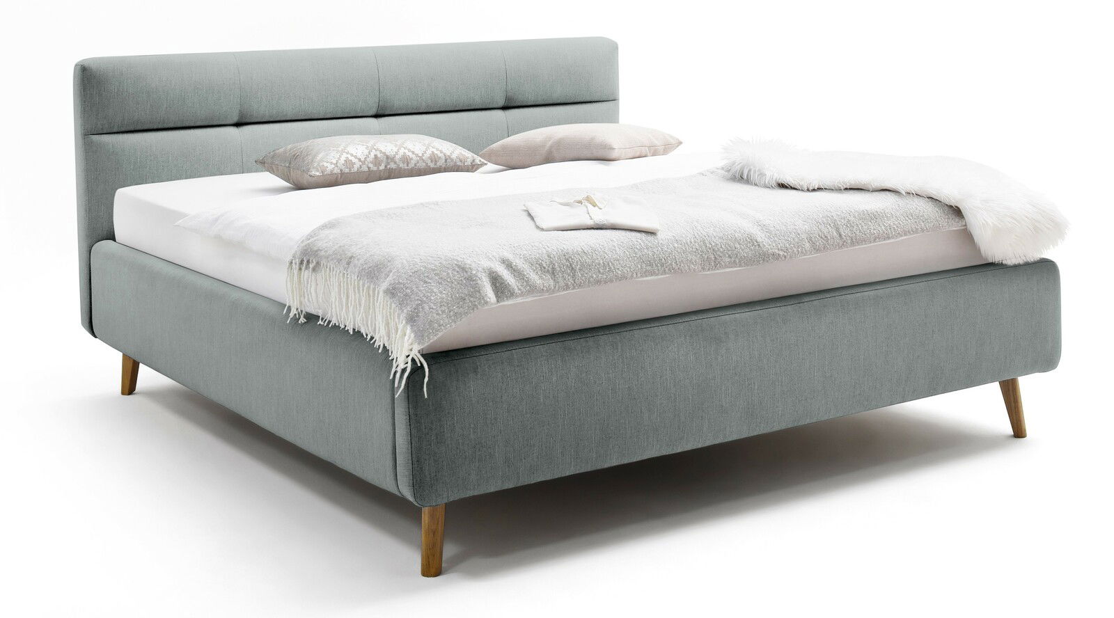 Graues Polsterbett mit Holzfüßen, seitliche Perspektive, dekoriert mit Kissen und Decken.