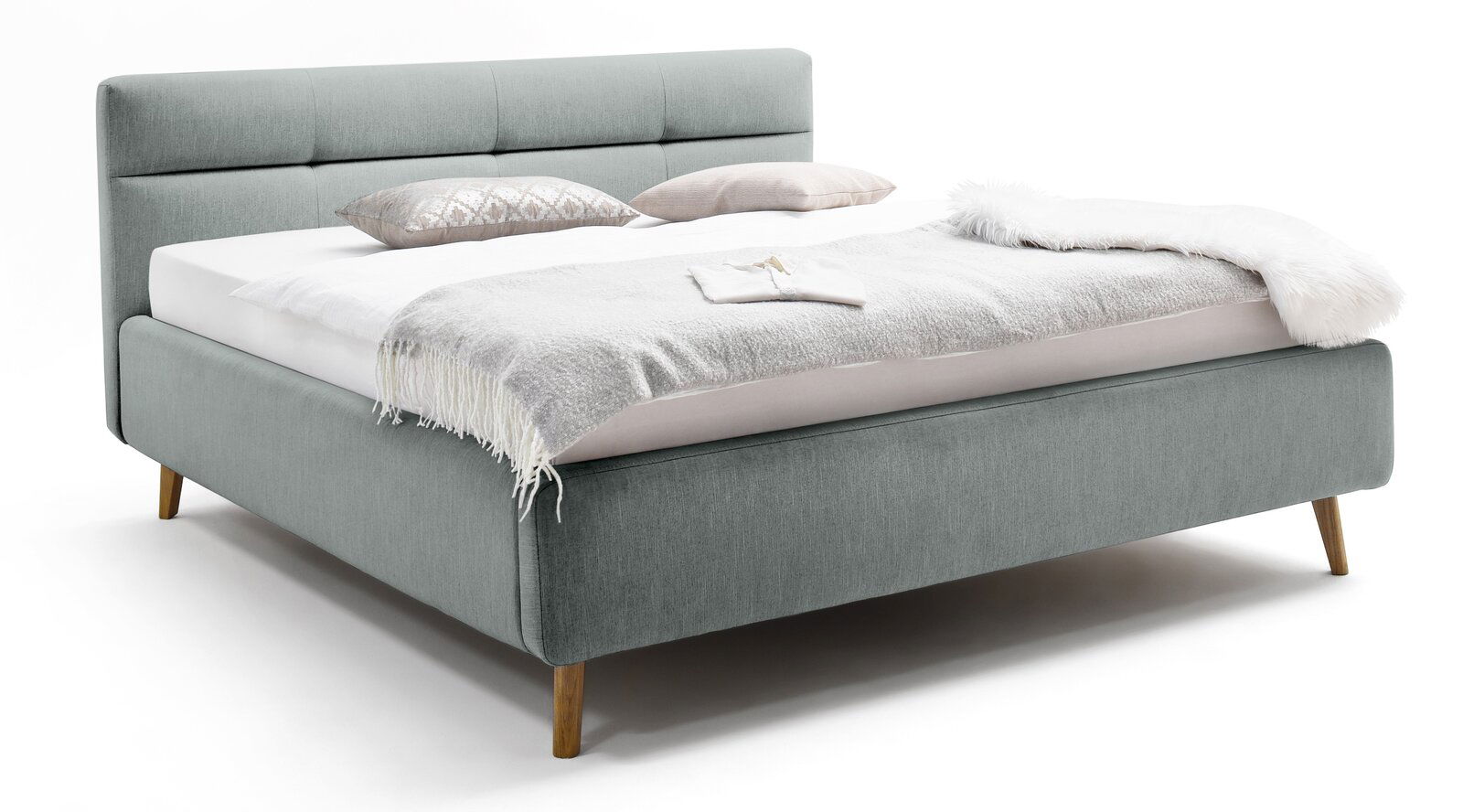 Graues Polsterbett mit Holzfüßen, seitliche Perspektive, dekoriert mit Kissen und Decken.