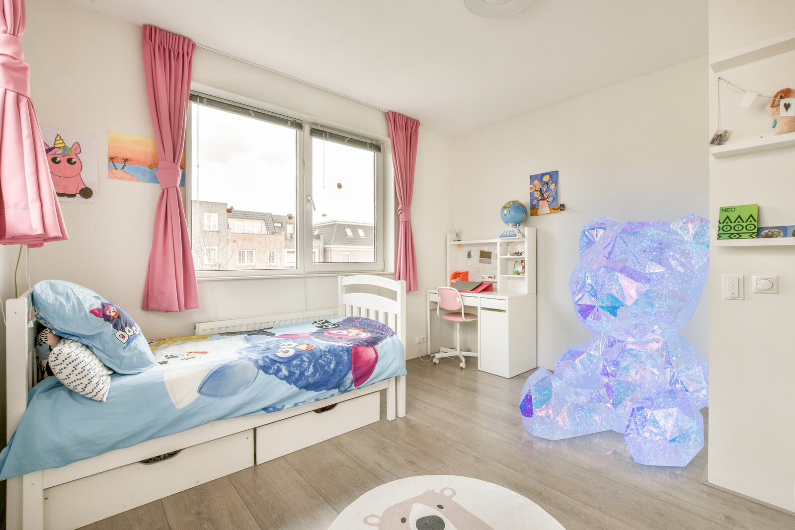Helles Kinderzimmer mit weißem Einzelbett und blauem Bettbezug, rosa Vorhängen am Fenster sowie weißem Schreibtisch mit rosa Stuhl; Blick aus einer Ecke des Raums in Richtung Fenster und Arbeitsbereich.