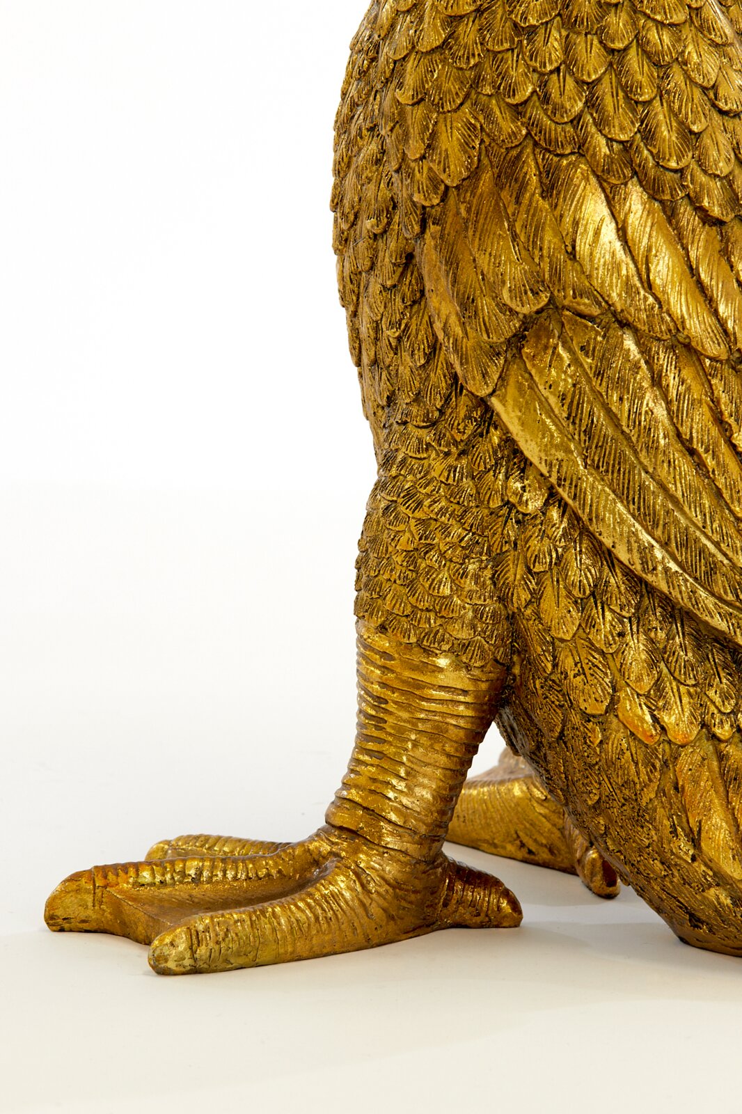 Detailansicht eines goldenen Tischleuchtenfußes in Form eines Vogels mit detaillierten Federn und Krallen.