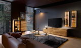 Modernes Wohnzimmer mit einem Highboard aus Holz, einem großen Fernseher auf einem Sideboard und zwei beleuchteten Hängeregalen an der Wand. Perspektive von der Seite.