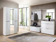 Moderne garderobe-inrichting met een witte hoogglanskast, spiegel, garderobepaneel en bank in een lichte ruimte met grote ramen, zijaanzicht.