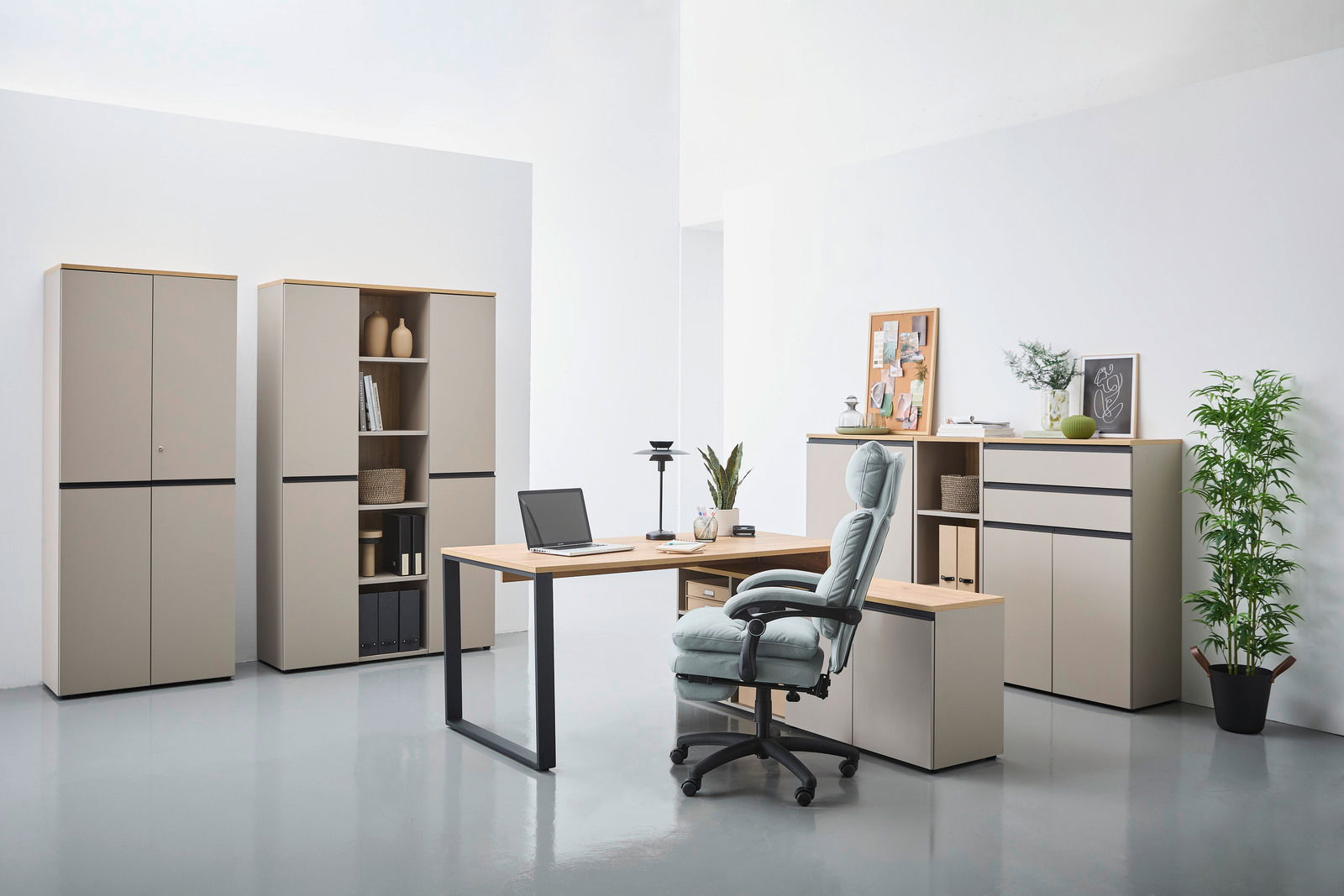 Moderne Büromöbel in einem hellen Raum, bestehend aus einem Winkelschreibtisch mit Laptop, mehreren Aktenschränken und einem ergonomischen Bürostuhl. Perspektive von vorne.