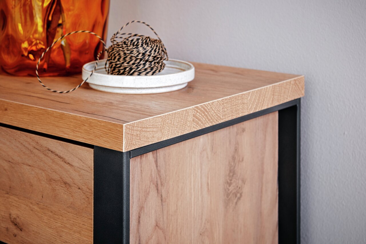 Close-up van een houten dressoir met een zwart metalen frame, met daarop een oranje vaas en een schaal met touw, gezien van bovenaf.