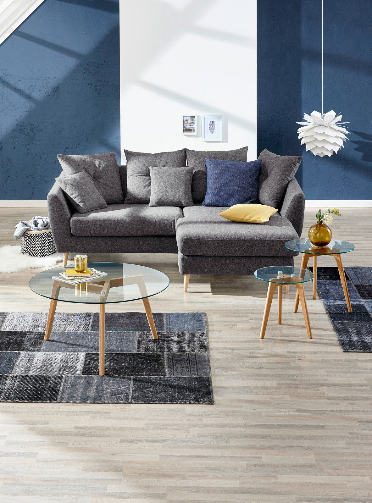 Graue Rundecke mit mehreren Kissen, fotografiert aus einer frontalen Perspektive in einem modern eingerichteten Wohnzimmer mit blauen Akzenten.