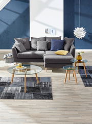 Graue Rundecke mit mehreren Kissen, fotografiert aus einer frontalen Perspektive in einem modern eingerichteten Wohnzimmer mit blauen Akzenten.