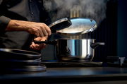 Mann öffnet einen dampfenden Schnellkochtopf aus Edelstahl in einer modernen Küche, seitliche Perspektive.