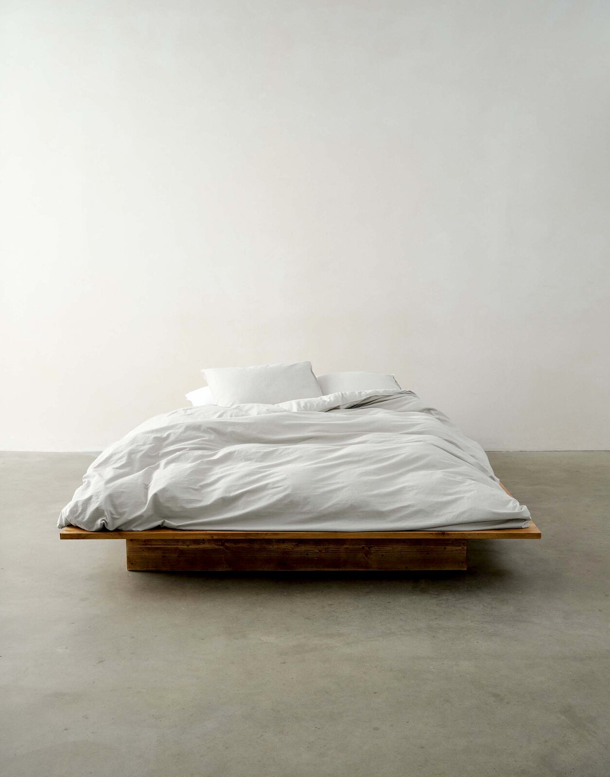 Bett mit weißer Bettwäsche auf einem Holzrahmen, frontal fotografiert