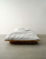 Bett mit weißer Bettwäsche auf einem Holzrahmen, frontal fotografiert