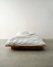 Bett mit weißer Bettwäsche auf einem Holzrahmen, frontal fotografiert