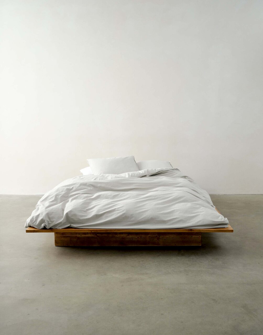 Bett mit weißer Bettwäsche auf einem Holzrahmen, frontal fotografiert