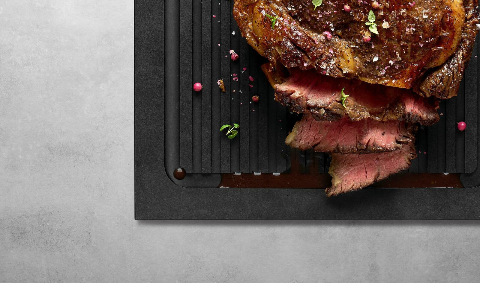 Schneidebrett mit Rillen, darauf saftiges, geschnittenes Fleisch, von oben betrachtet.