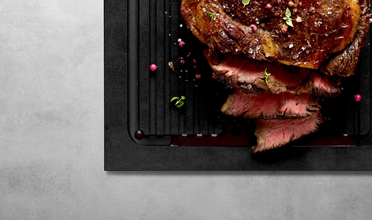 Schneidebrett mit Rillen, darauf saftiges, geschnittenes Fleisch, von oben betrachtet.