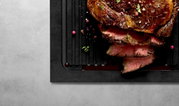 Schneidebrett mit Rillen, darauf saftiges, geschnittenes Fleisch, von oben betrachtet.