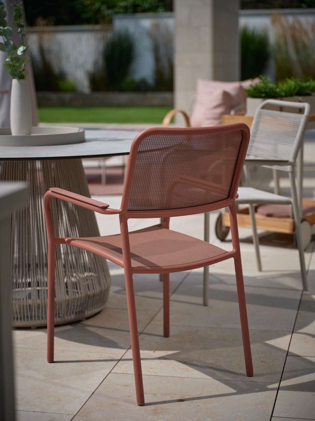 Roter Stapelsessel aus Metall mit Armlehnen, seitliche Perspektive auf einer Terrasse neben einem runden Tisch.