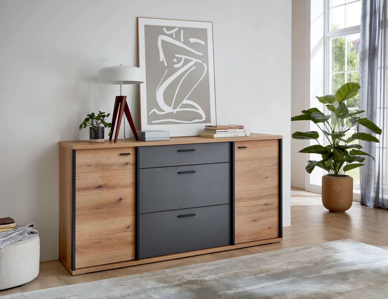 XORA Dressoir MELO Moderne ladekast/dressoir in houtlook met antracietkleurige fronten en zwarte handgrepen, gepresenteerd vanuit een licht schuin perspectief in de lichte woonkamer