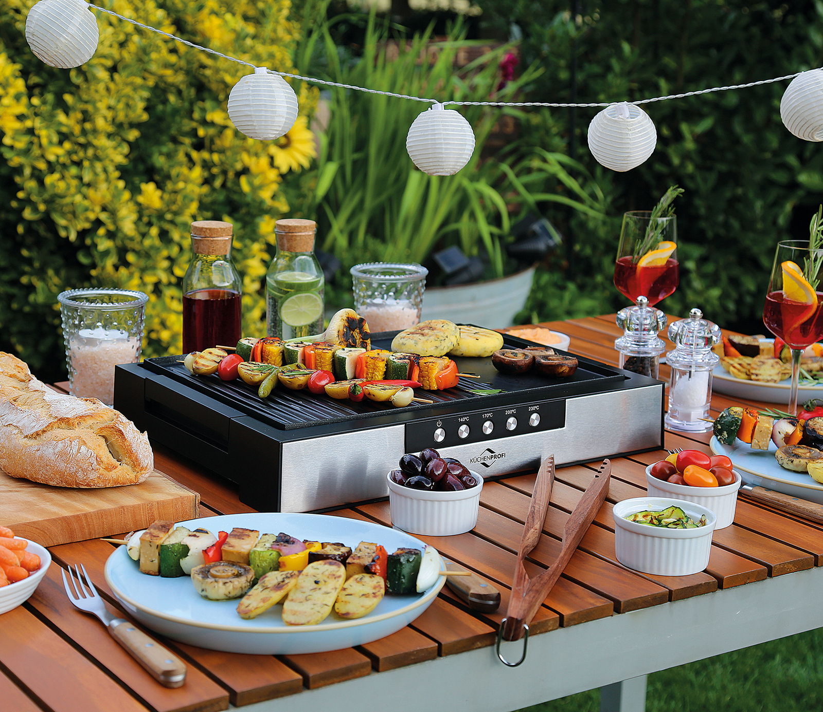 KÜCHENPROFI Tischgrill STYLE Tischgrill Style auf einem Holztisch im Garten, umgeben von frischem Gemüse und Getränken, aus der Vogelperspektive fotografiert.