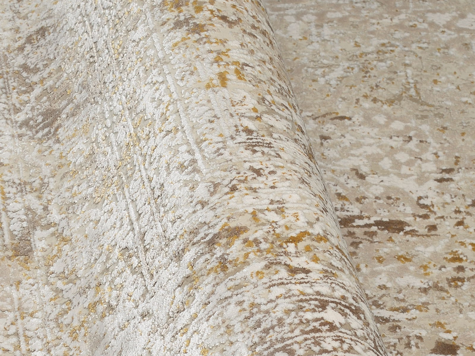 Nahaufnahme eines Designer-Teppichs mit abstraktem Muster in Beige- und Goldtönen, perspektivisch von der Seite aufgenommen.