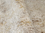 Nahaufnahme eines Designer-Teppichs mit abstraktem Muster in Beige- und Goldtönen, perspektivisch von der Seite aufgenommen.
