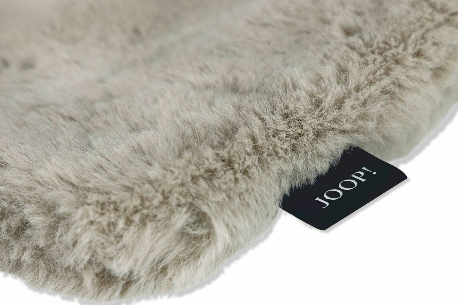 Nahaufnahme einer flauschigen, beigen Decke mit einem schwarzen Etikett, das 'JOOP!' zeigt.