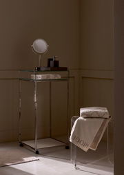 Elegantes Gästetuch in einem stilvollen Badezimmer, auf einem transparenten Stuhl drapiert, mit einem modernen, minimalistischen Design. Perspektive von der Seite.