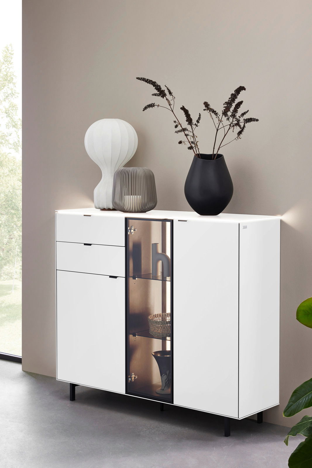 Modernes weißes Highboard mit Glastür und dekorativen Vasen, seitliche Perspektive