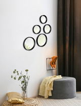 Fünf rund angeordnete Spiegel an einer weißen Wand, mit schwarzem Rahmen, in einem modernen Wohnambiente. Perspektive von der Seite.