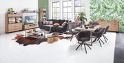Moderne Wohnzimmermöbel in einem hellen Raum mit großen Fenstern, bestehend aus einer Vitrine, einem TV-Lowboard, einem Couchtisch und einem Esstisch mit Stühlen, aus der Perspektive des gesamten Raumes betrachtet.
