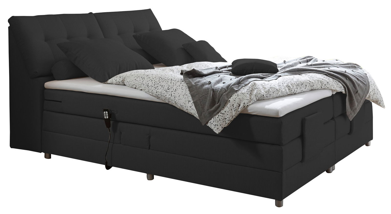 Schwarzes Boxspringbett mit mehreren Kissen und einer gemusterten Decke, seitliche Perspektive