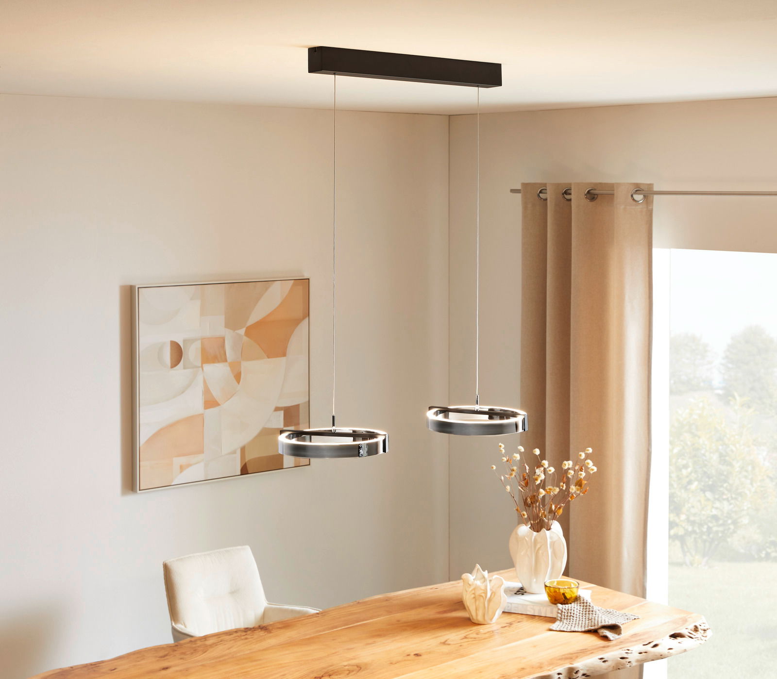 Moderne LED-Hängeleuchte mit zwei runden Leuchtringen, von der Decke hängend über einem Esstisch, seitliche Perspektive.