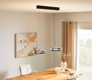 Moderne LED-Hängeleuchte mit zwei runden Leuchtringen, von der Decke hängend über einem Esstisch, seitliche Perspektive.