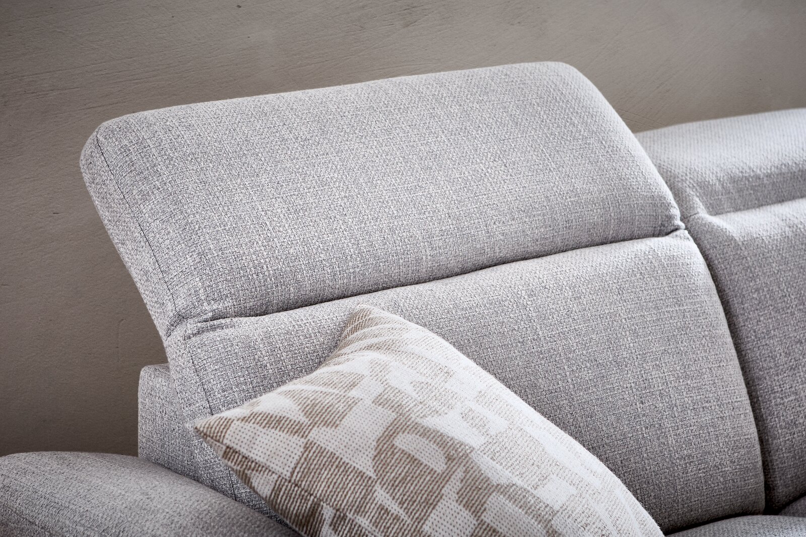 Nahaufnahme eines grauen Longchairs mit verstellbarer Kopfstütze und einem gemusterten Kissen, seitliche Perspektive.