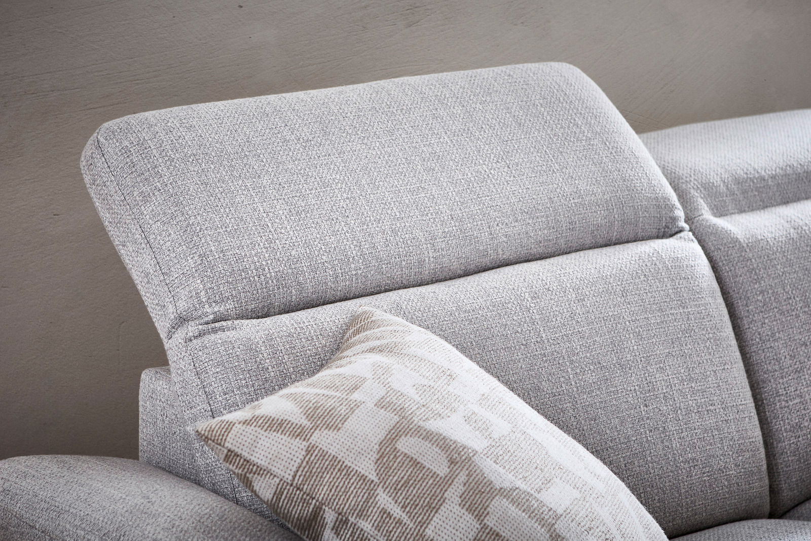 Nahaufnahme eines grauen Longchairs mit verstellbarer Kopfstütze und einem gemusterten Kissen, seitliche Perspektive.
