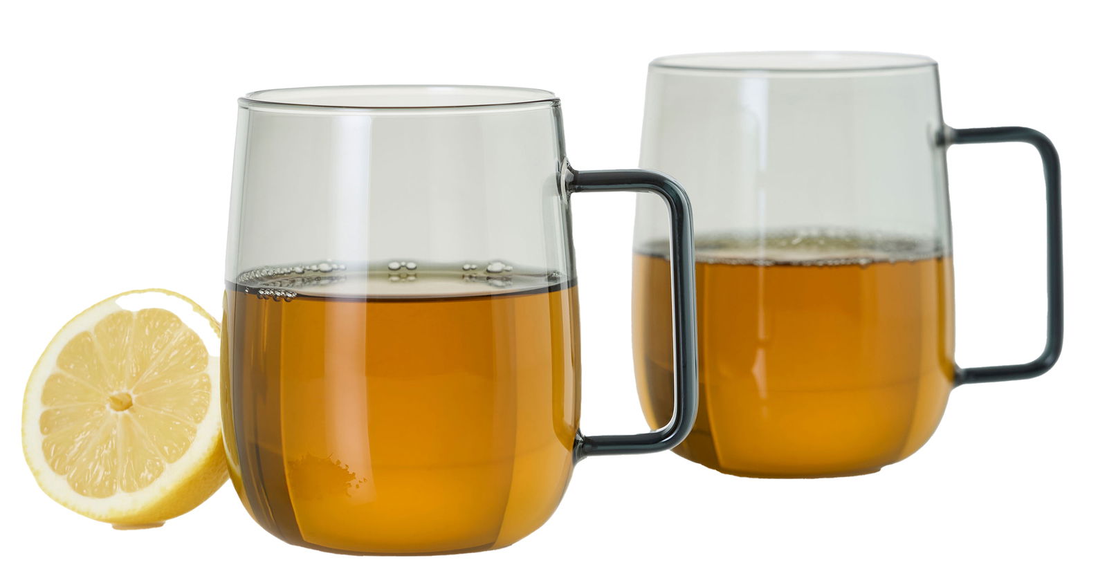 Ad Hoc Tassen 2-tlg. YUNA Zwei transparente Tassen mit schwarzem Griff, gefüllt mit Tee, im Vordergrund eine halbe Zitrone, seitliche Perspektive.
