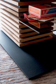 Nahaufnahme eines modernen Couchtischs mit gestapelten Holzelementen und einer Glasplatte, seitliche Perspektive.