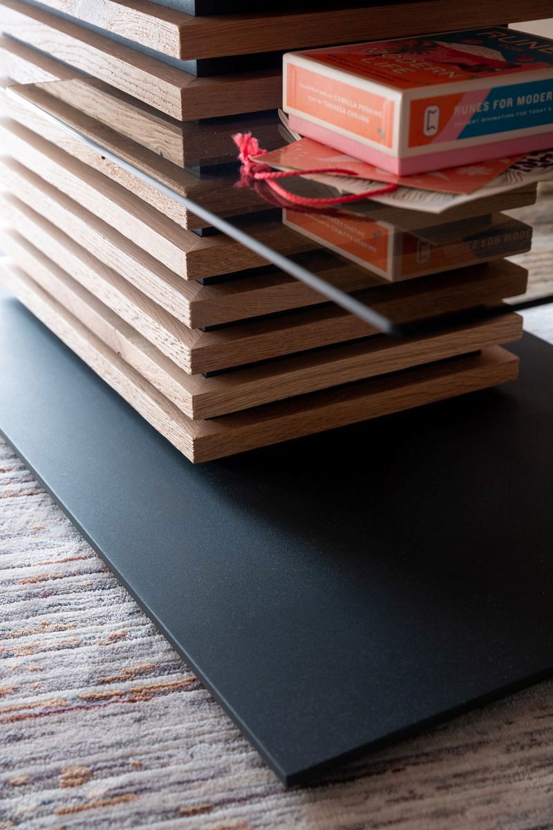 Nahaufnahme eines modernen Couchtischs mit gestapelten Holzelementen und einer Glasplatte, seitliche Perspektive.