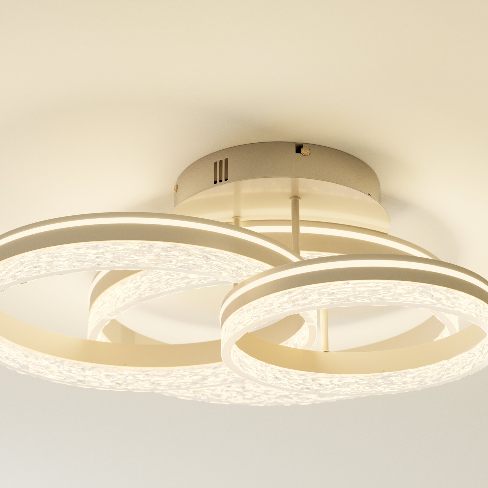 Moderne LED-Deckenleuchte mit drei leuchtenden, verschlungenen Ringen in Weiß und kristallartiger Struktur, warmweißes Licht, Ansicht von unten (Untersicht) an der Decke montiert