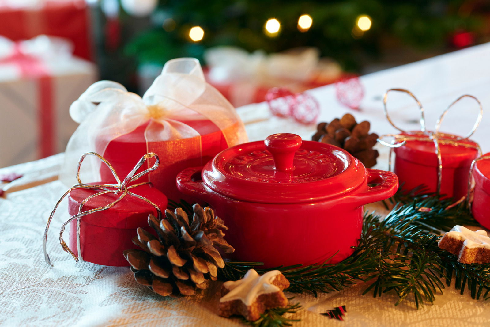 Rote Mini-Cocotte auf einem festlich dekorierten Tisch mit Tannenzweigen und Weihnachtsgebäck, seitliche Perspektive