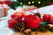 Rote Mini-Cocotte auf einem festlich dekorierten Tisch mit Tannenzweigen und Weihnachtsgebäck, seitliche Perspektive